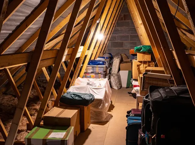 Attic full of boxes and bags under exposed rafters before a cleanout