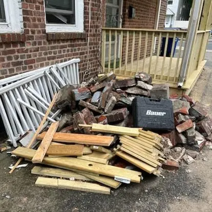 Torn-out railings, lumber and brick stacked on a driveway after a porch demolition