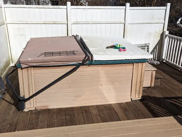 Old hot tub with a brown cover sitting on a wooden deck before removal