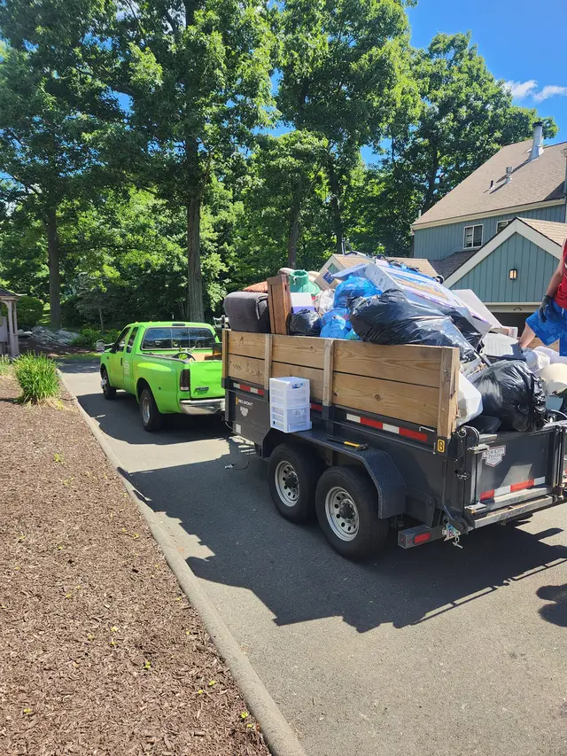 Green pickup truck towing a trailer loaded with bagged junk