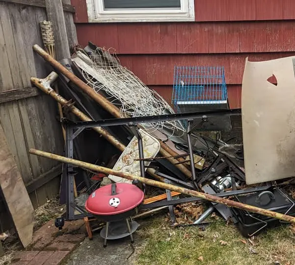 Pile of old grills, metal and lumber beside a red house, ready for junk removal